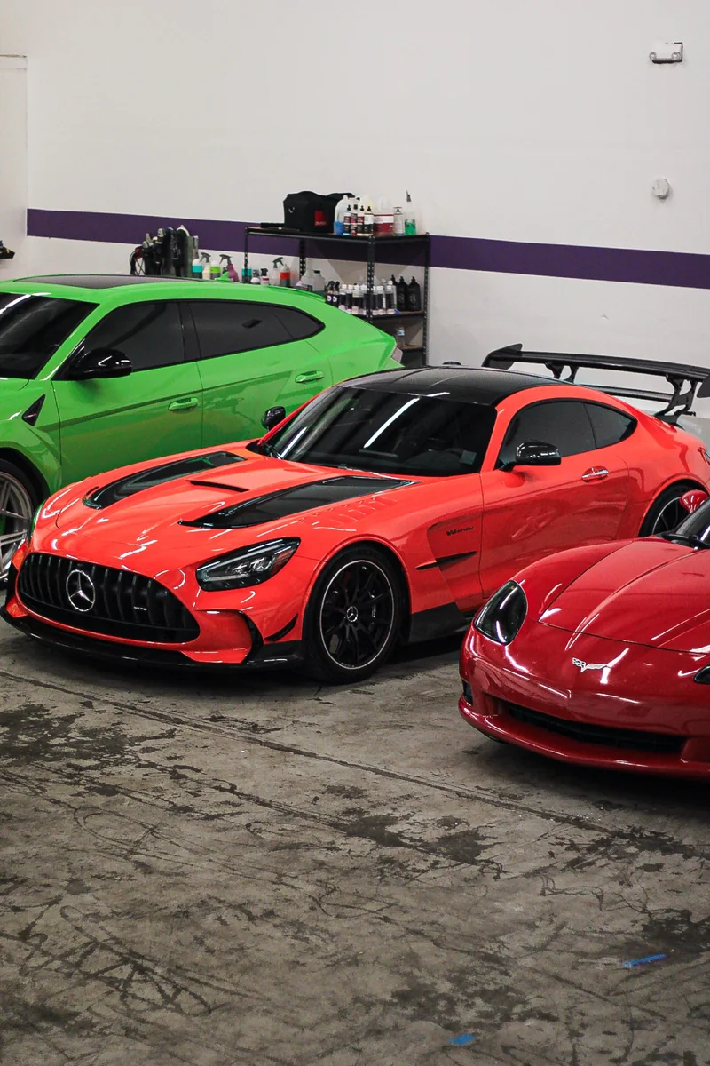 An AMG GT Black Series, a Corvette and a green Urus parked side by side on a detail shop floor